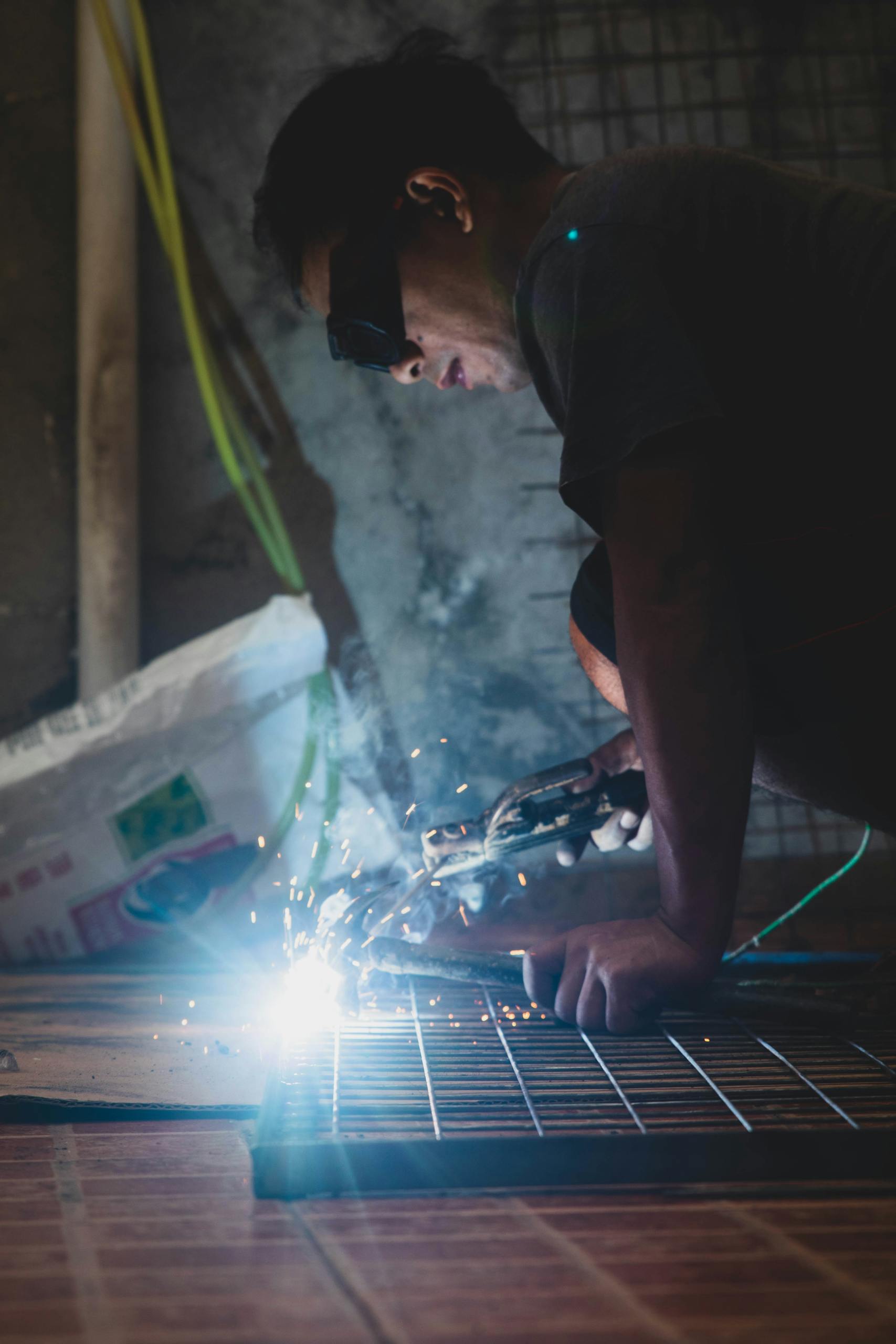 An adult male welder using protective eyewear, focused on welding metal with sparks flying.